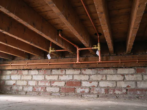 New copper main along the basement joists of a Chicago two-flat, splitting into two branches with tagged shutoff valves rising to the floor above