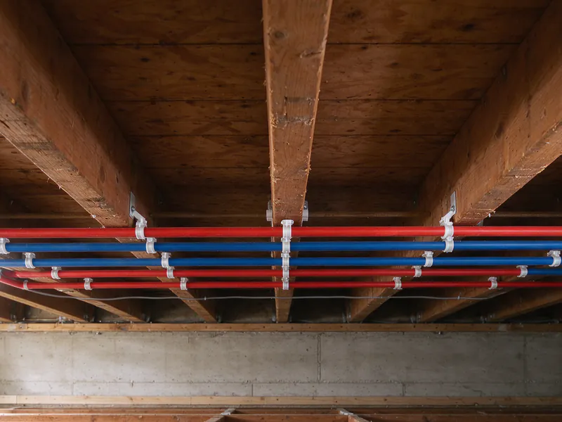 Red and blue PEX lines running across the underside of floor joists in white plastic clips